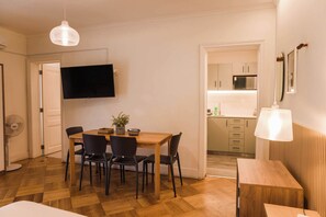 Ein kompakter Wohnraum mit Essbereich, einer Küche und einem an der Wand befestigten Fernseher.
