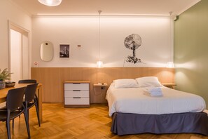 A hotel room with a bed, bedside table, lamp, wall art, and a desk with a chair. - Studio Oasis | Near Bellavista and Hospitals (Providencia)