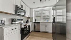 Una cocina moderna con armarios blancos, electrodomésticos de acero inoxidable, horno empotrado y lavavajillas.