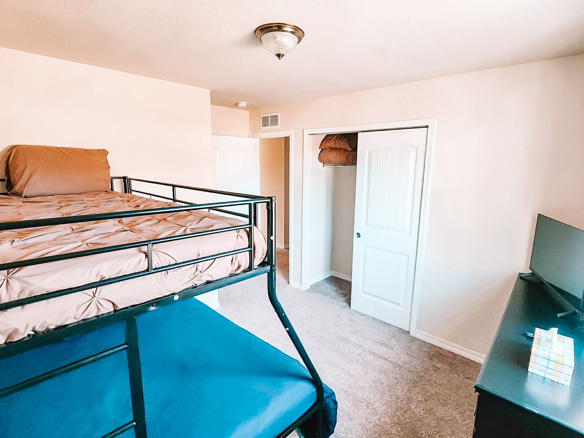 A dormitory room with bunk beds, a desk, a chair, a wardrobe, and a door.