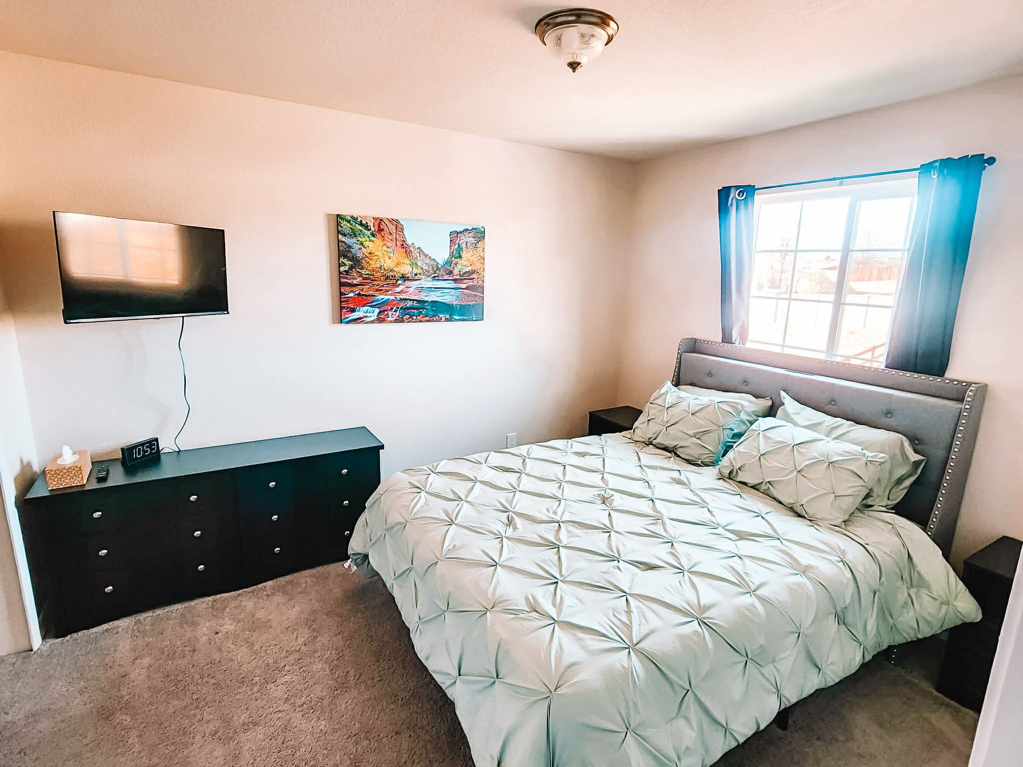 A bedroom with a bed, a dresser, a TV mounted on the wall, and a painting.