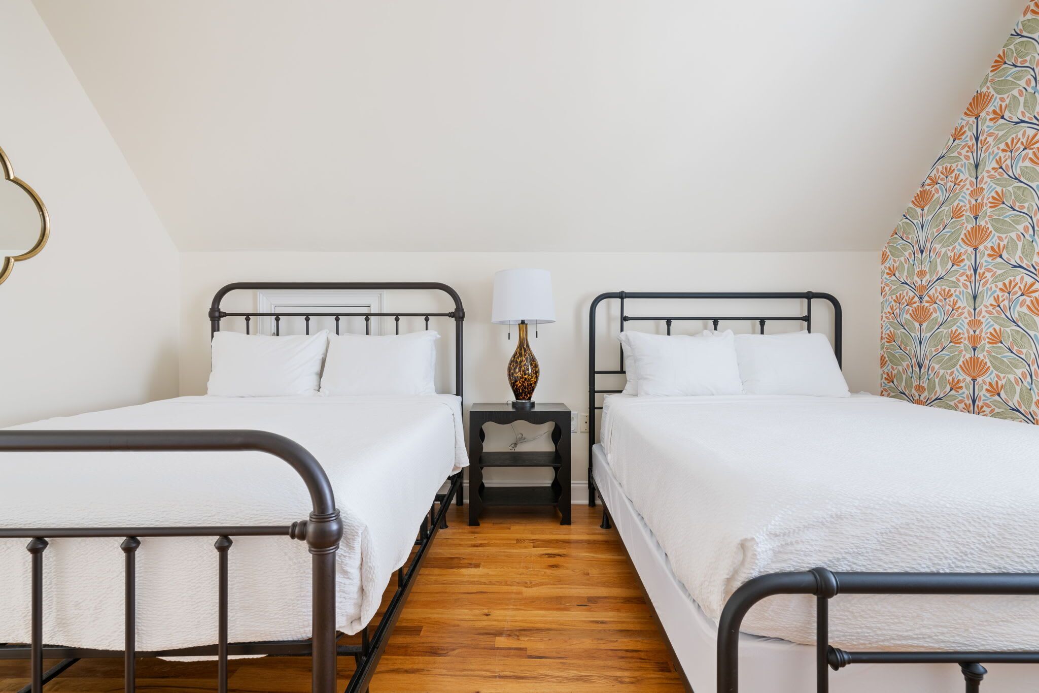 A bedroom with two single beds, a nightstand with a lamp, and a patterned curtain.