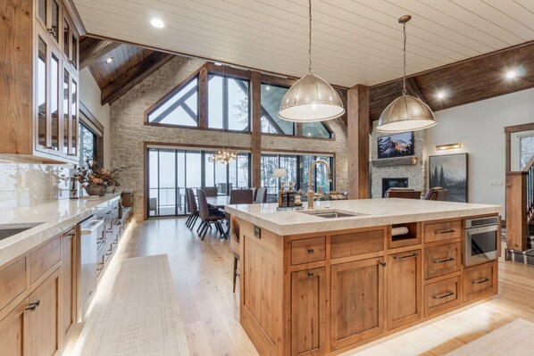 A spacious kitchen with a large island, wooden cabinets, and a stone wall. - Stillwater Retreat | Waterfront + Private Dock (Island Park)