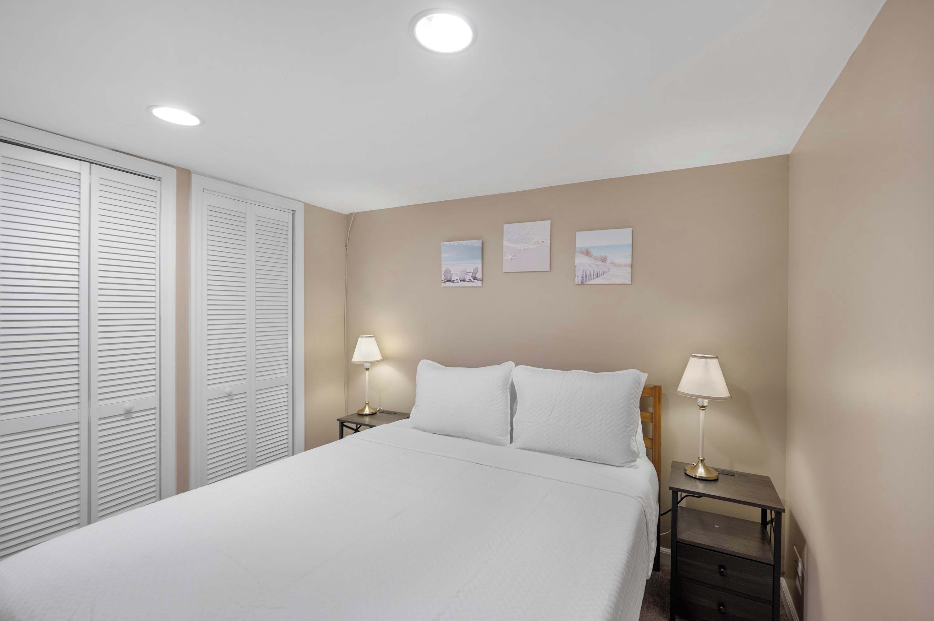 A bedroom with a bed, two bedside tables with lamps, a closet with sliding doors, and three wall-mounted pictures.