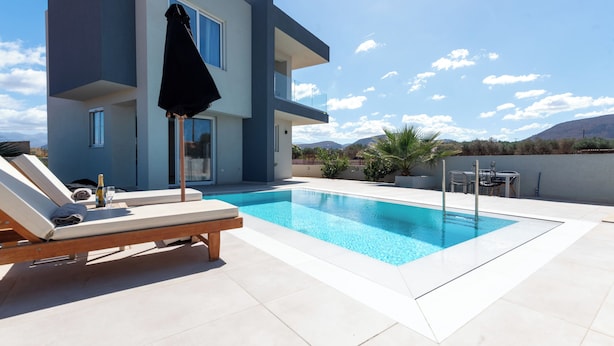 Un bâtiment moderne doté d’une piscine, de chaises longues et d’une table avec des chaises.