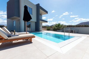 En modern byggnad med en pool, solstolar och ett bord med stolar.