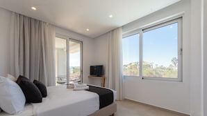 Une chambre d’hôtel moderne avec un grand lit, un téléviseur posé sur une petite table et un balcon offrant une vue sur les palmiers.
