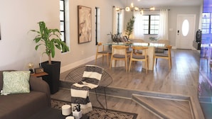 Ein modernes Wohnzimmer mit einem Glastisch, Holzstühlen, einer Couch und einem Blumentopf.