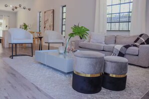 A modern living room with a grey sofa, white armchairs, a glass coffee table, and two grey ottomans with gold accents. - Enjoyable 3-bedroom house with AC in vibrant Miami (Miami)
