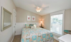 A bedroom with a bed, a ceiling fan, a bedside lamp, a window with blinds, and a door. - Coconut cottage unit 2! (Holmes Beach)