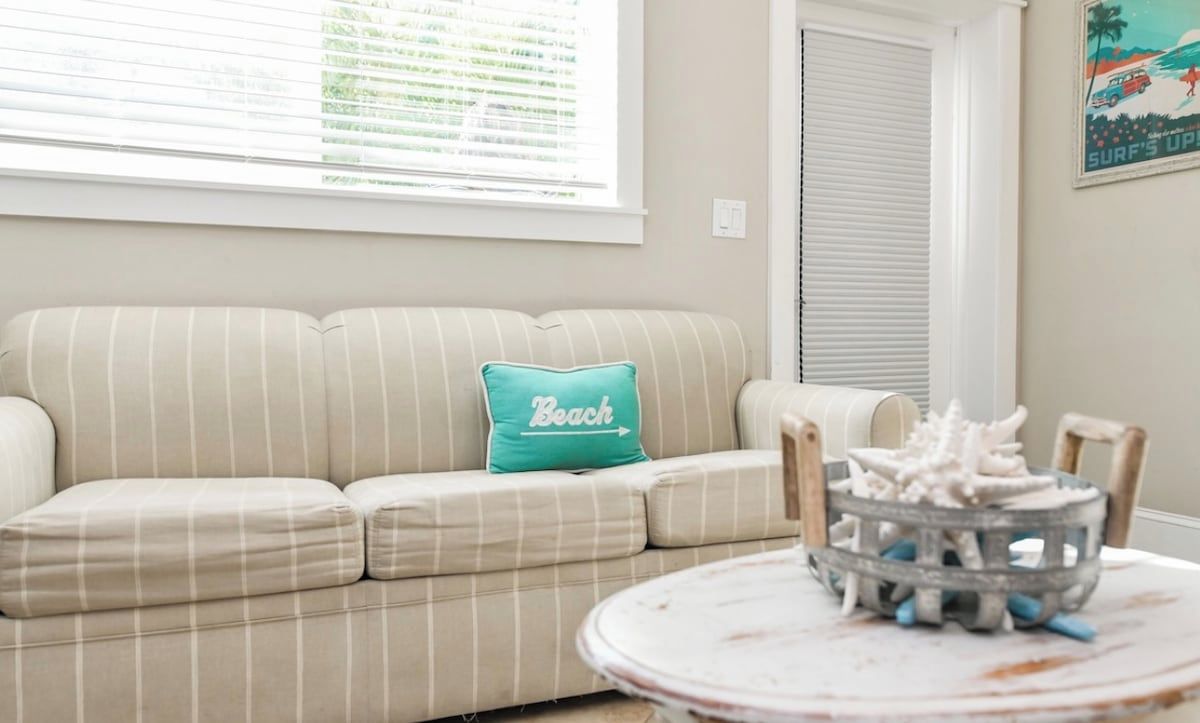 A beige-striped sofa with a teal pillow, a round table with a decorative item, and a window with blinds.