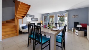Ein Essbereich mit einer Holztreppe, einem Esstisch mit Stühlen, einem Fernseher und einem Sofa.