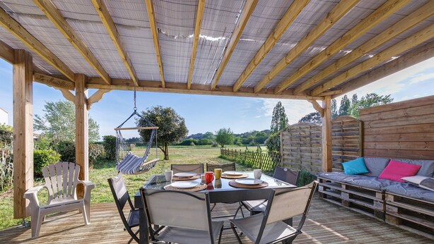 Eine Terrasse im Freien mit einer Hollaube, einem Esstisch mit Stühlen, einer Hängematte und einer Couch mit Kissen.