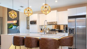 Una cocina moderna con una isla central, electrodomésticos de acero inoxidable y una zona de bar con taburetes de cuero.
