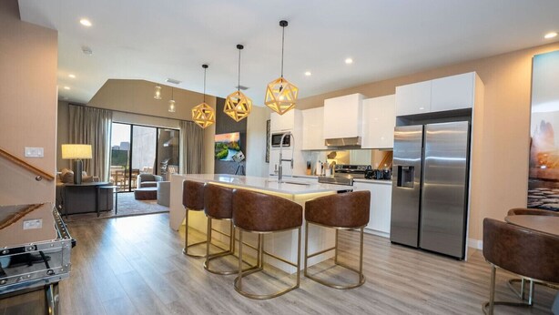 Una cocina moderna con una isla central, taburetes de bar, electrodomésticos de acero inoxidable e iluminación colgante.