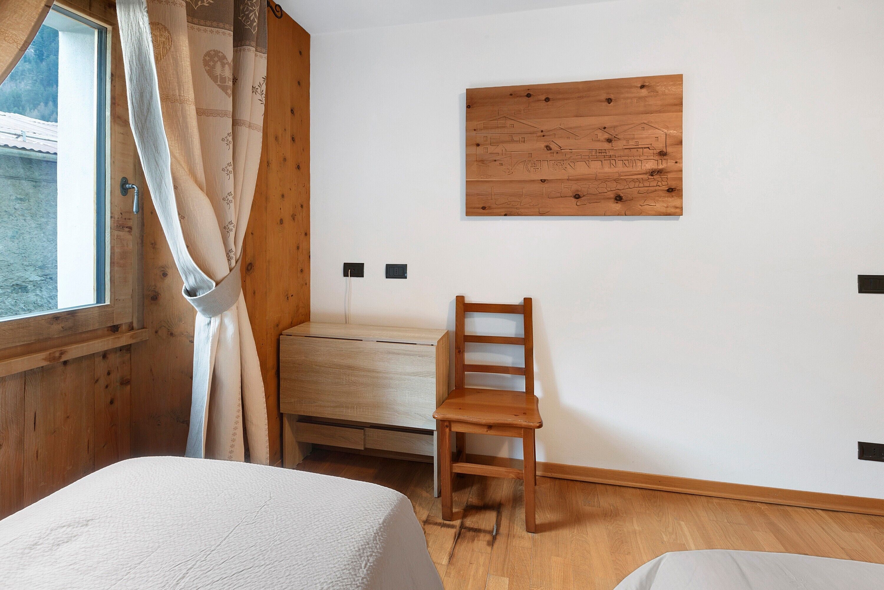 Une pièce comprenant un lit, une chaise en bois, un bureau et une fenêtre avec des rideaux.