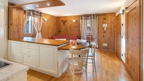 A kitchen with wooden walls, a wooden island, white cabinets, and a dining area with a red bench.