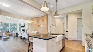 A modern kitchen with a central island, pendant lighting, and a view of the outdoors. - Kiawah Exclusives | 4 Airy Hall (Kiawah Island)
