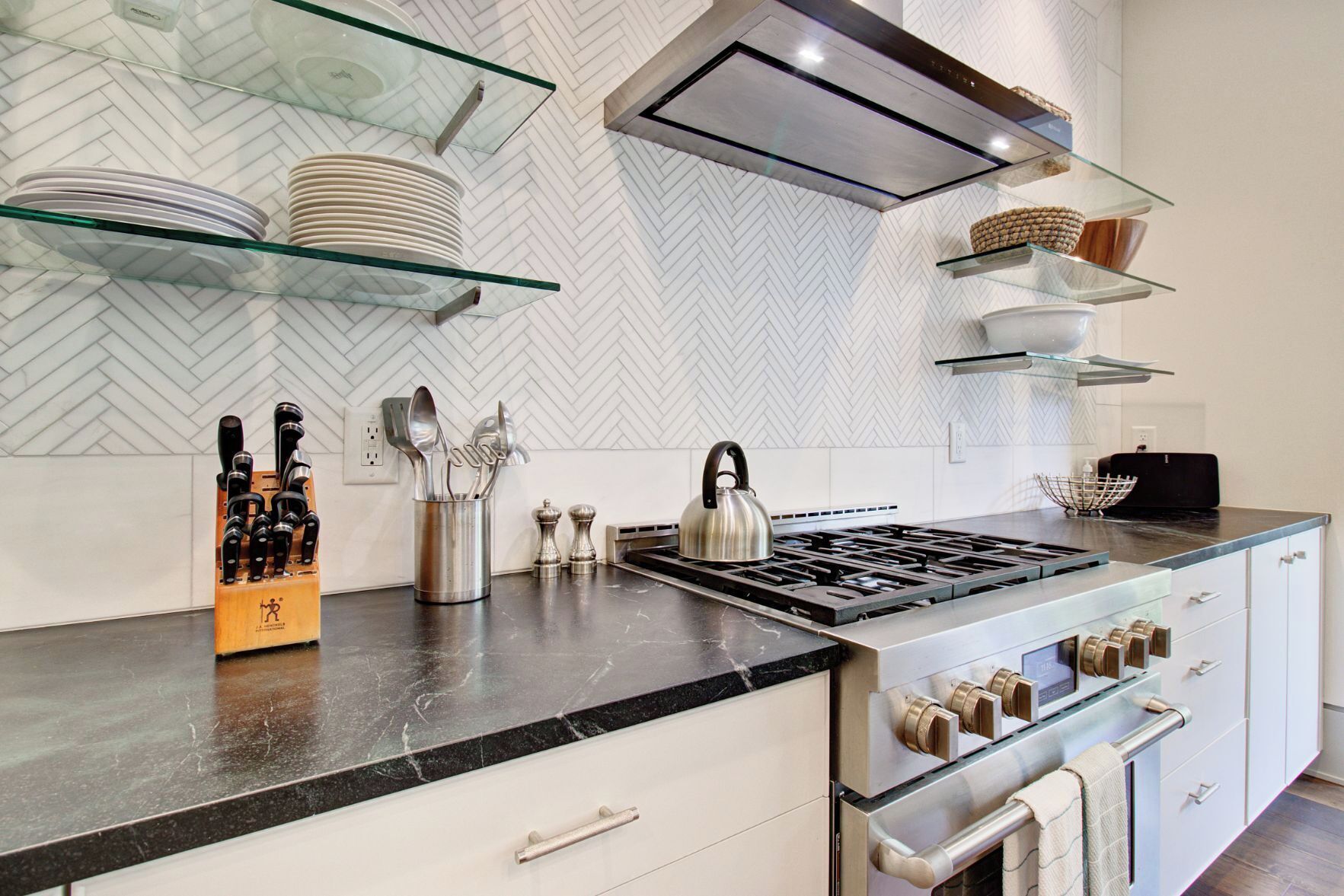 A modern kitchen with a gas stove, stainless steel appliances, and glass shelves.