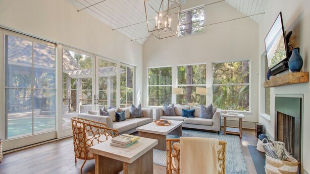 A spacious living room with large windows, a fireplace, and a pool view. - Kiawah Exclusives | 4 Airy Hall (Kiawah Island)