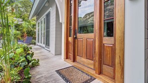 A wooden front door with a glass panel, a porch with a wooden floor, and a doormat. - Kiawah Exclusives | 4 Airy Hall (Kiawah Island)