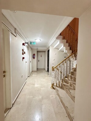 A hotel hallway with a marble floor, a staircase with glass balusters, and a fire extinguisher on the wall. - HOTEL EFENDİ (Istanbul)