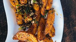 A white rectangular plate with roasted potatoes garnished with herbs and spices, accompanied by a blue fork on a dark wooden surface. - Hotel peace and happy (Bhimeshwar)