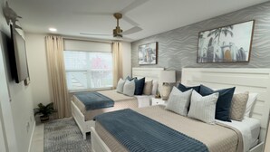 Ein modernes Schlafzimmer mit zwei Betten, einem Deckenventilator, einem Fernseher und einem Fenster mit Vorhängen.
