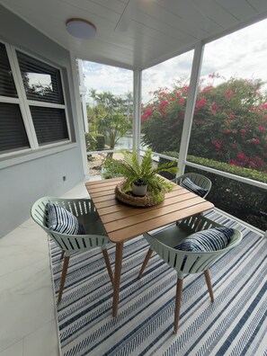 A covered patio with a wooden table and two chairs, surrounded by a patterned rug. - Newly renovated and beautifully decorated 2 bedroom 2 bath condo (Siesta Key)