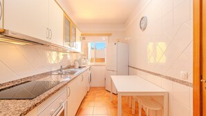 Una cocina con armarios blancos, horno empotrado, pileta y comedor con mesa y sillas.
