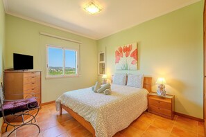 A bedroom with a bed, a dresser, a chair, a nightstand with a lamp, and a painting on the wall.