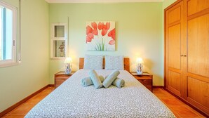 Un dormitorio con cama, dos lámparas de noche, una ventana, un armario de madera y un cuadro en la pared.