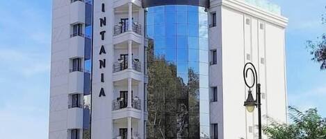 A multi-story hotel with a modern facade, balconies on each floor, and a reflective glass section.