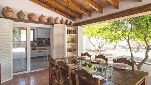 A dining area with a wooden table and chairs, a kitchen in the background, and a view of trees and a clear sky. - Villa 'Valls' with Private Pool, Wi-Fi and Air Conditioning (Montuïri)