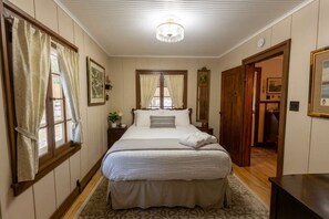 A bedroom with a large bed, a chandelier, a window with curtains, and a door leading to another room. - Charming Craftsman Cottage, Walk to Beach (Douglas)