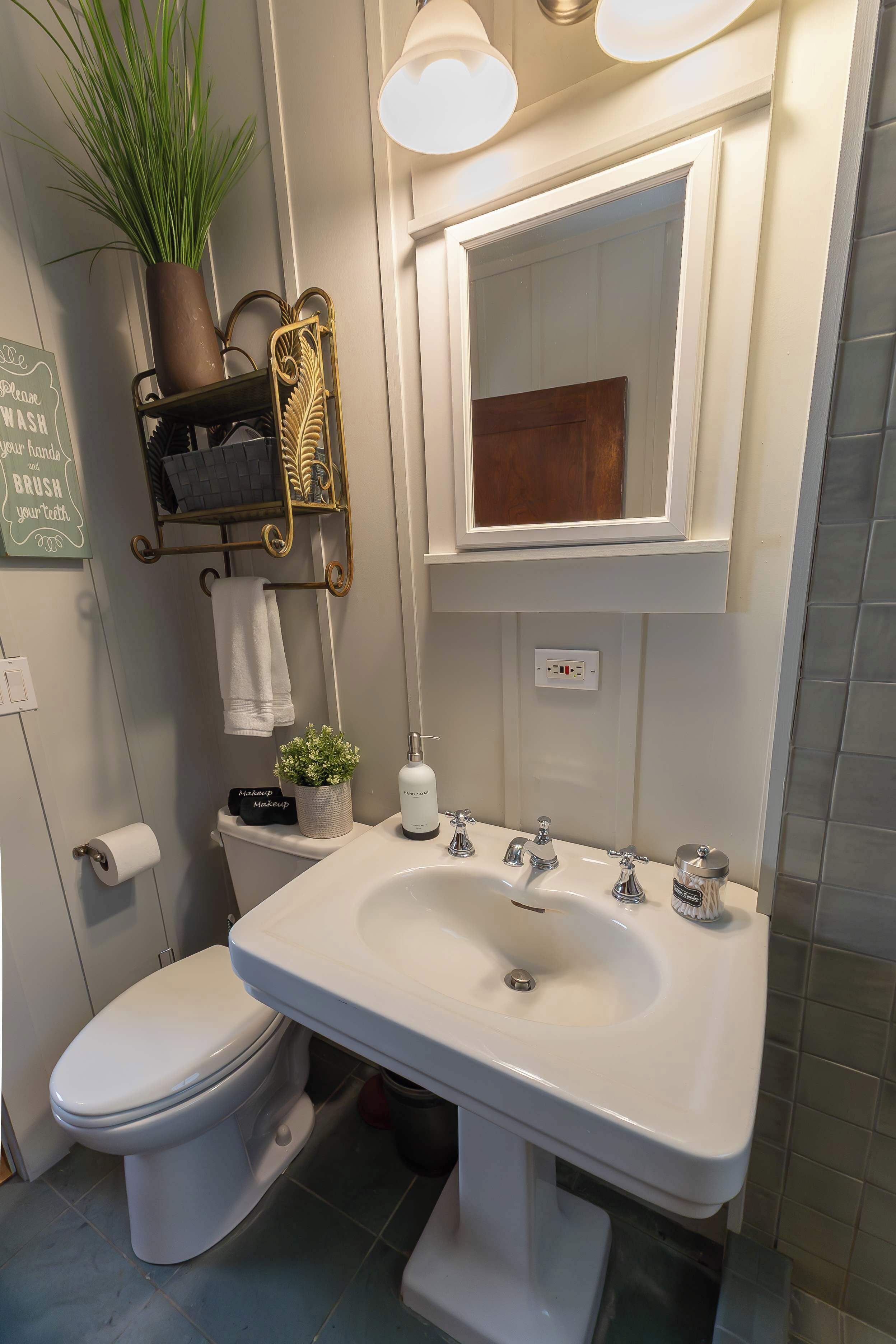A bathroom with a white sink, a toilet, a towel rack, a potted plant, and a mirror.