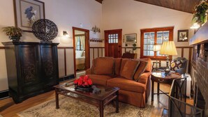 Una sala de estar acogedora con techo de madera, un sofá marrón, una mesa de centro de vidrio con un centro decorativo rojo y una alfombra estampada.