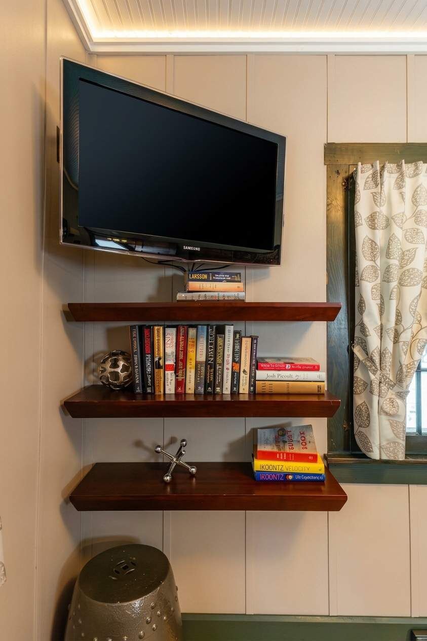 A wall-mounted television above a wooden shelf with books and a decorative metal object.