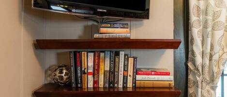 A wall-mounted television above a wooden shelf with books and a decorative metal object.