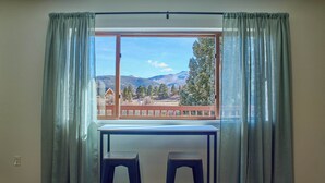Ein Zimmer mit Fenster und Blick auf eine Berglandschaft, einem Holztisch und zwei Stühlen.