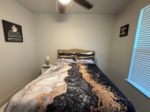 Une chambre à coucher comprenant un lit, une table de chevet, un ventilateur de plafond et deux éléments de décoration murale.