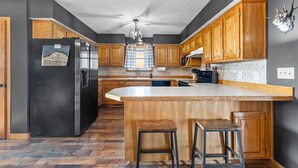 A kitchen with wooden cabinets, a black refrigerator, a large island with stools, and a chandelier. - Countryside Views | Sleeps 20, Hot Tub, Fire Pit (Theodosia)