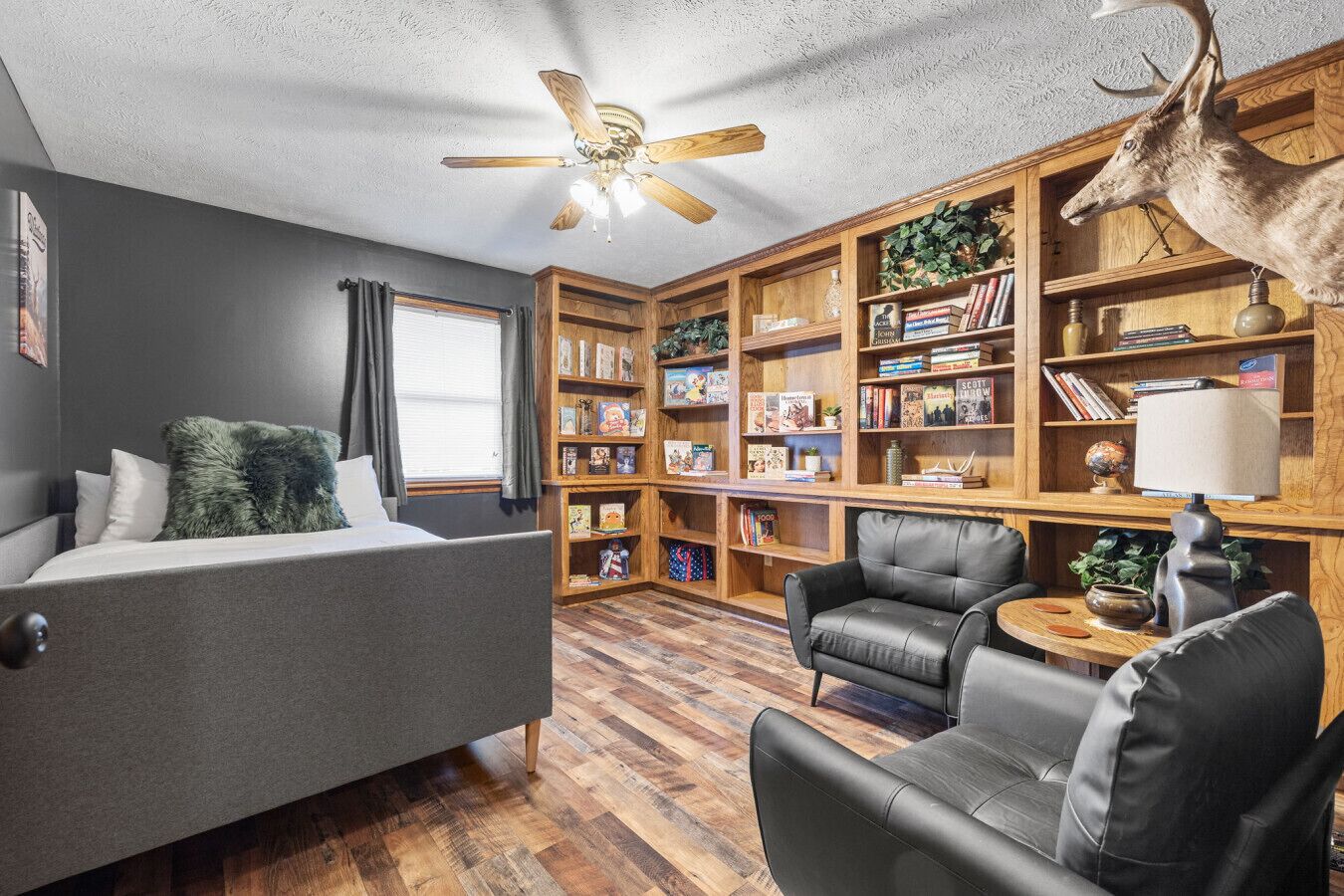 Une pièce confortable avec un lit, deux chaises, une bibliothèque et un ventilateur de plafond.