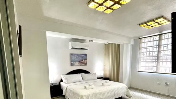 Une chambre spacieuse avec un grand lit, un appareil de climatisation et une fenêtre avec des rideaux.