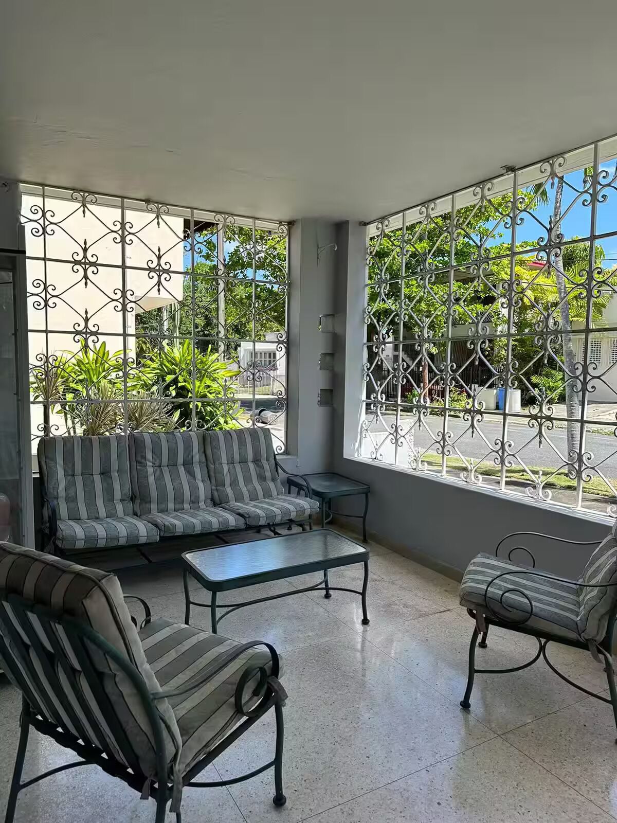 Un patio iluminado por el sol con un sofá a rayas, dos sillones y una pequeña mesa.