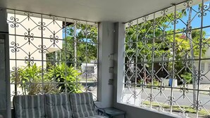 Une terrasse ensoleillée avec un canapé à rayures, deux fauteuils et une petite table.
