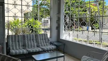 Un patio iluminado por el sol con un sofá a rayas, dos sillones y una pequeña mesa.