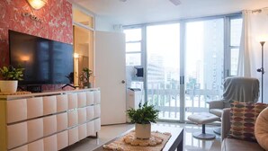 Un soggiorno moderno con televisione a schermo piatto, un divano, un tavolino da caffè e un balcone con vista sulla città.
