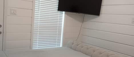 A bedroom with a bed, a television mounted on the wall, and a window with blinds.