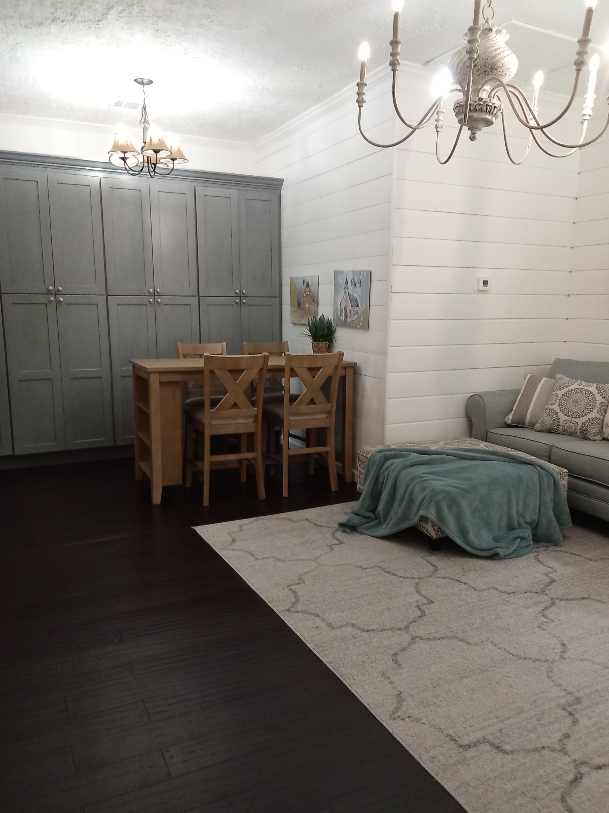 Une pièce comprenant une table à manger, des chaises, un lustre, un canapé et un tapis à motifs.